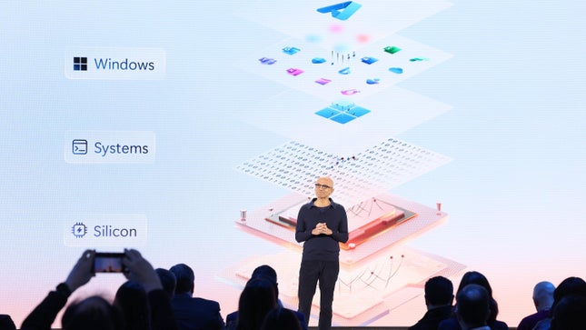 الرئيس التنفيذي لشركة مايكروسوفت، ساتيا ناديلا، يقف على خشبة المسرح محاطًا بأسماء شركتي WIndows Systems وSilicon